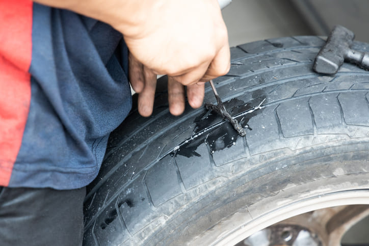 Tyre puncture being repaired by technician Tyre repair being performed using a plug tool on a punctured car tyre